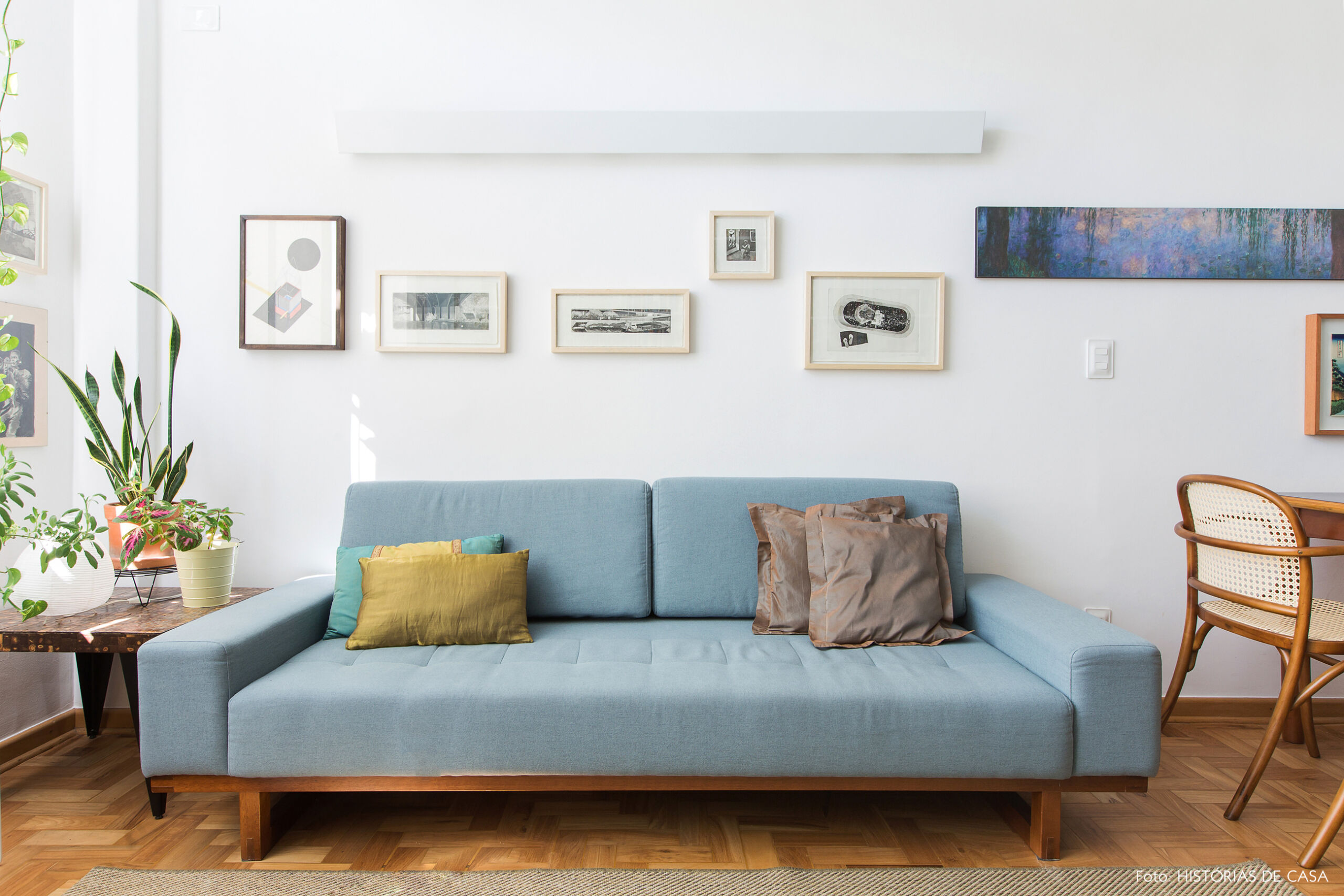 Sala pequena com sofá colorido, azul e parede de quadros