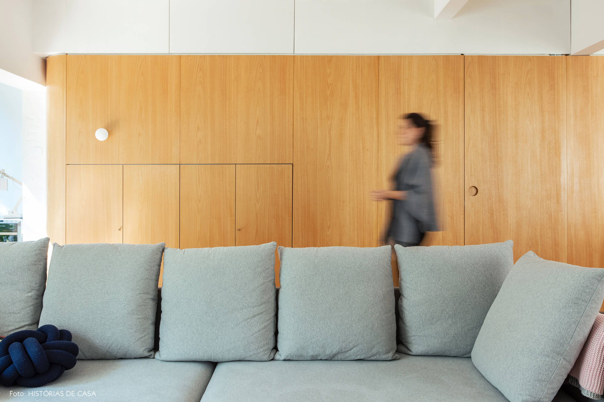 Sofá cinza neutro com painel de marcenaria ao fundo