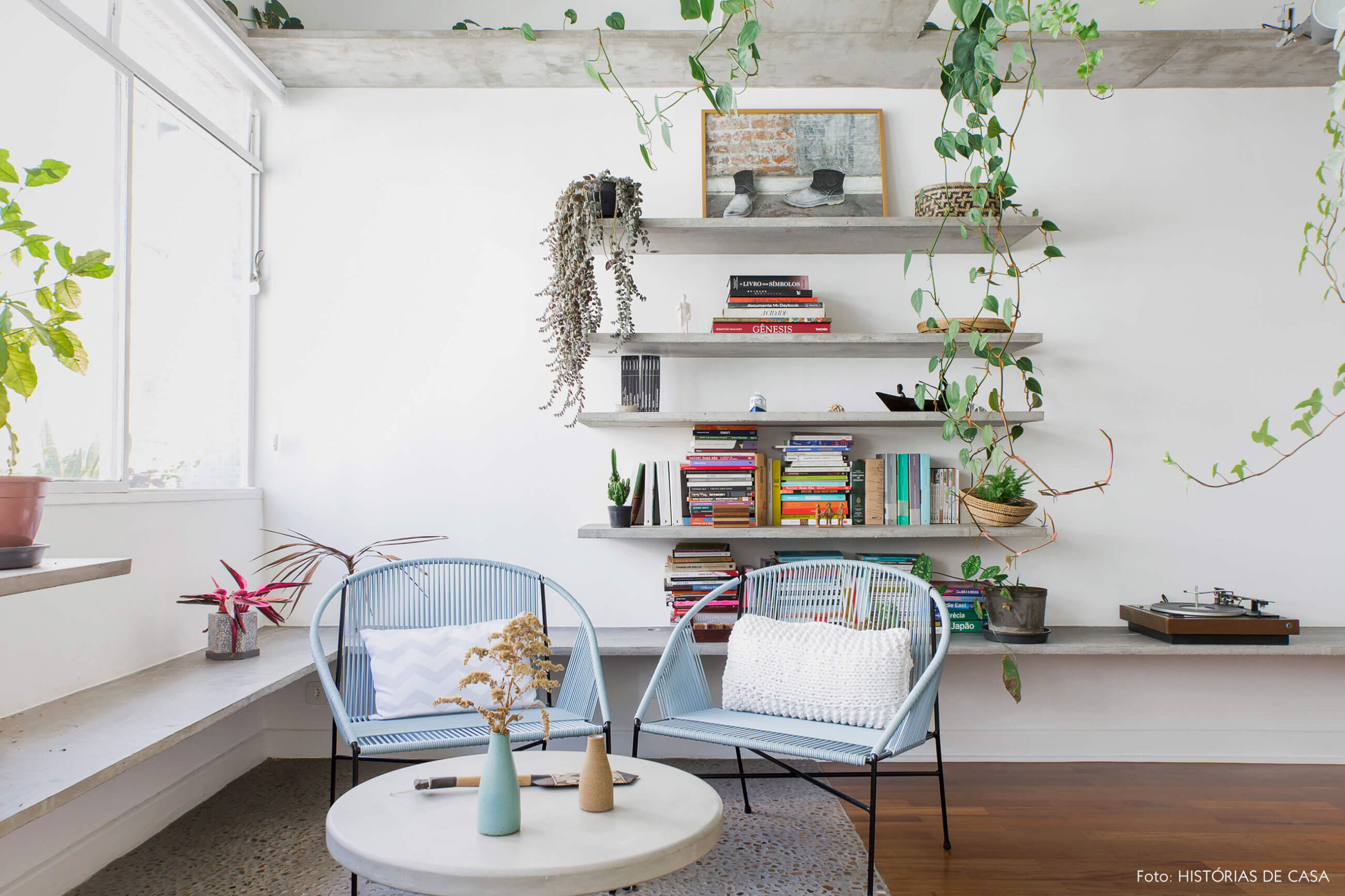 Sala com varanda integrada, piso de seixos e prateleiras de concreto com plantas