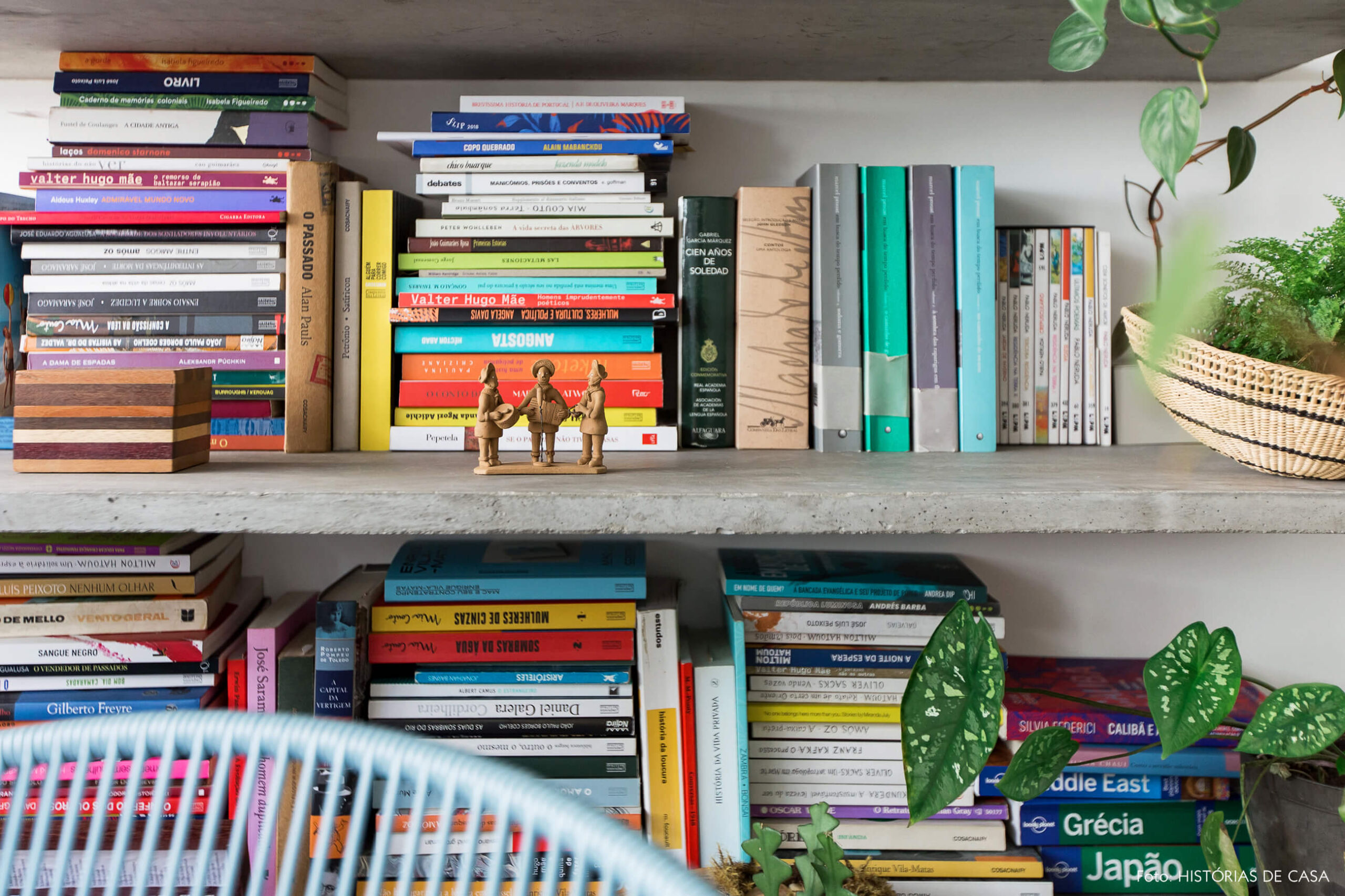 Sala com varanda integrada, piso de seixos e prateleiras de concreto com muitos livros