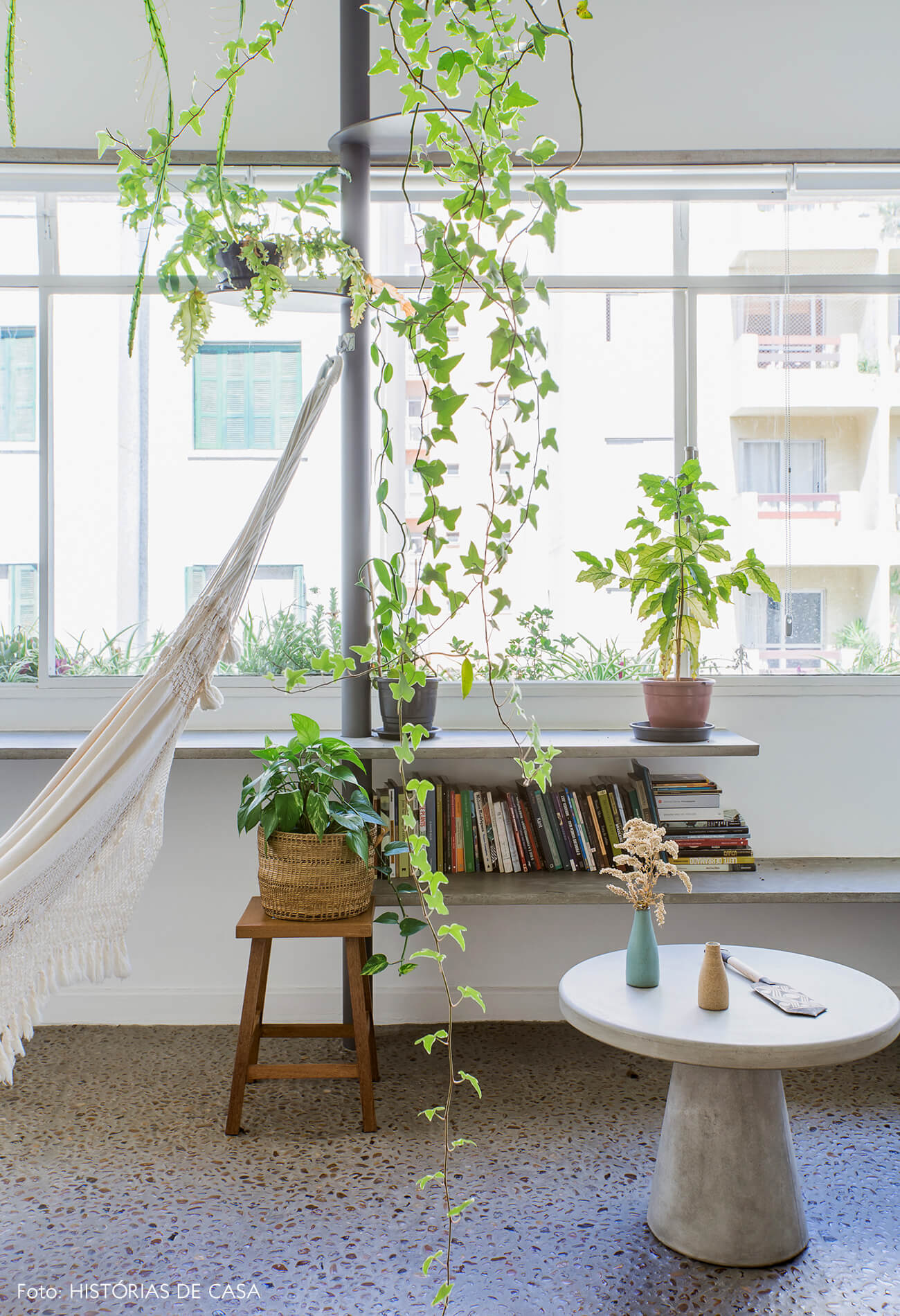 Sala com varanda integrada, prateleiras de concreto com plantas e rede de balanço