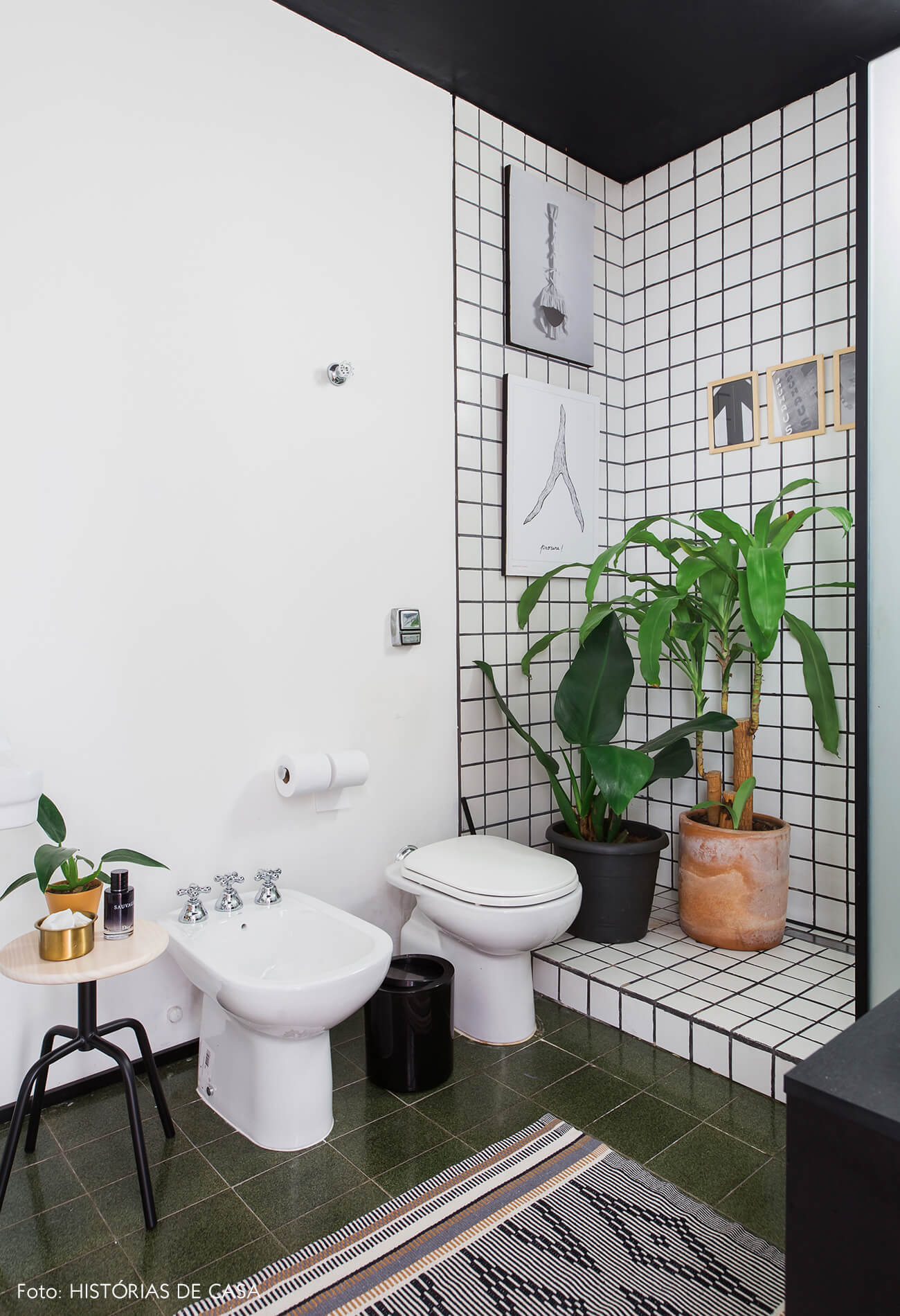 Banheiro com azulejos grid, teto pintado de preto e muitas plantas