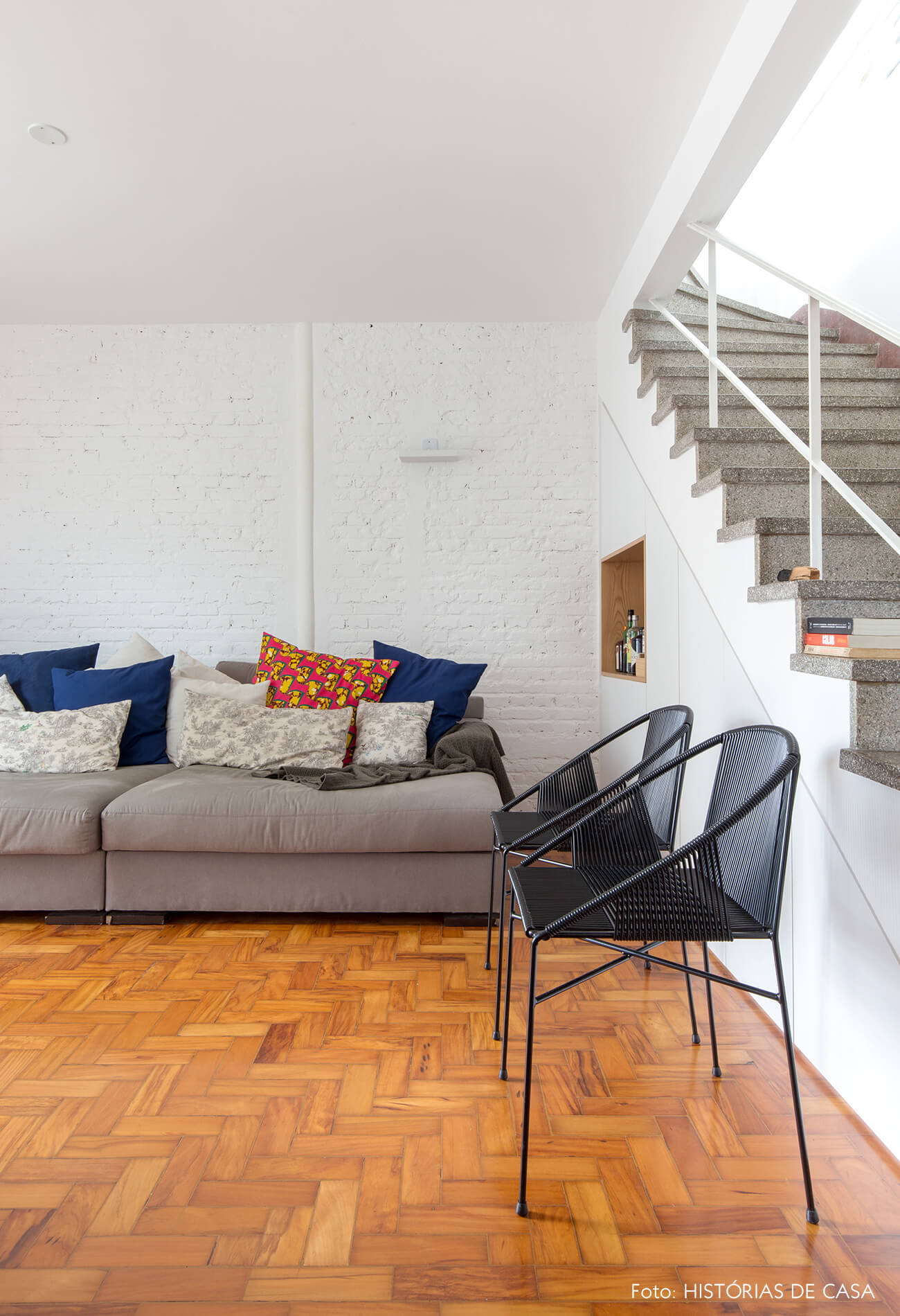 Sala com sofá cinza e parede de tijolinho branco
