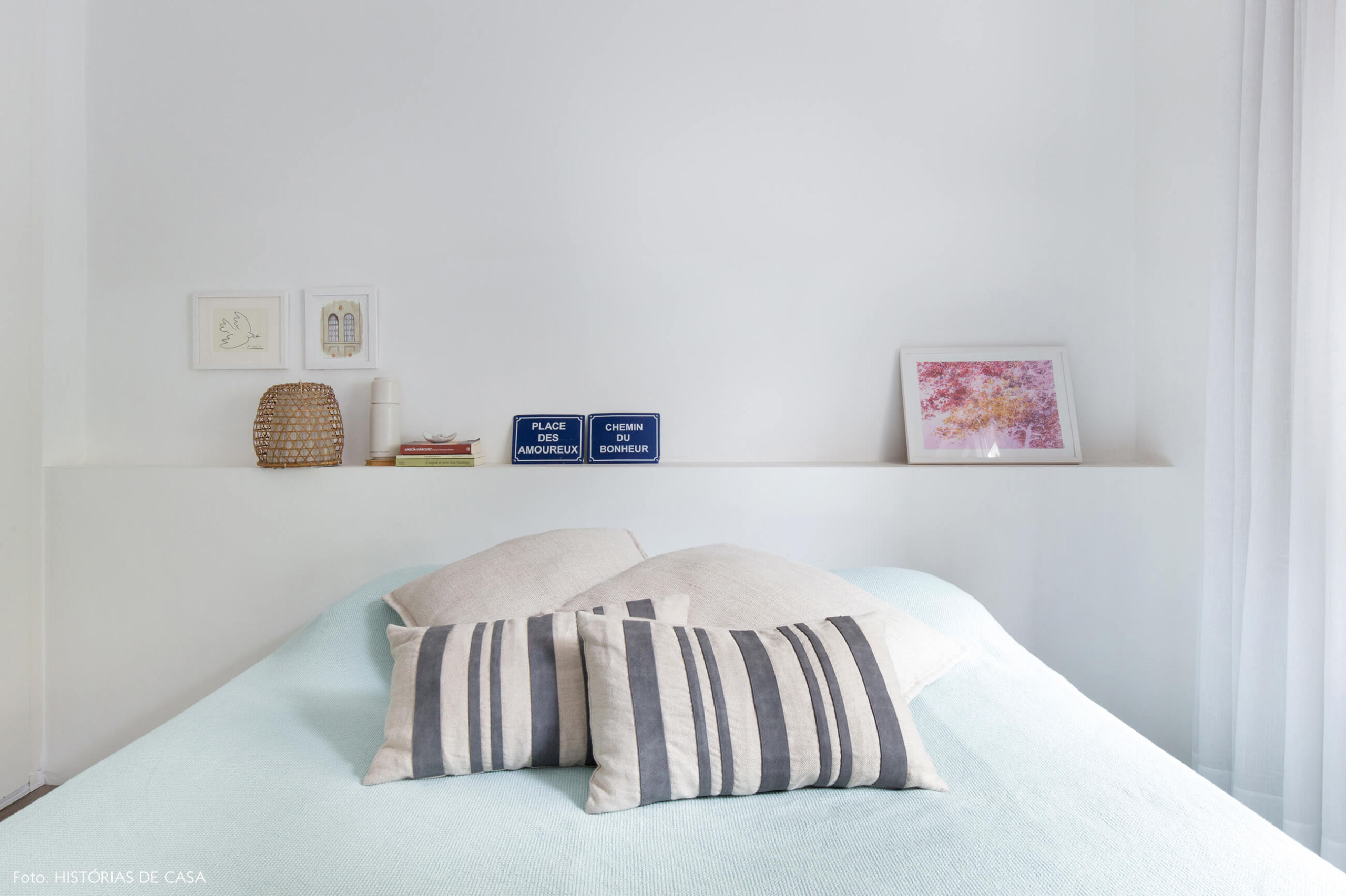 Quarto com tons neutros e cabeceira branca para apoiar objetos