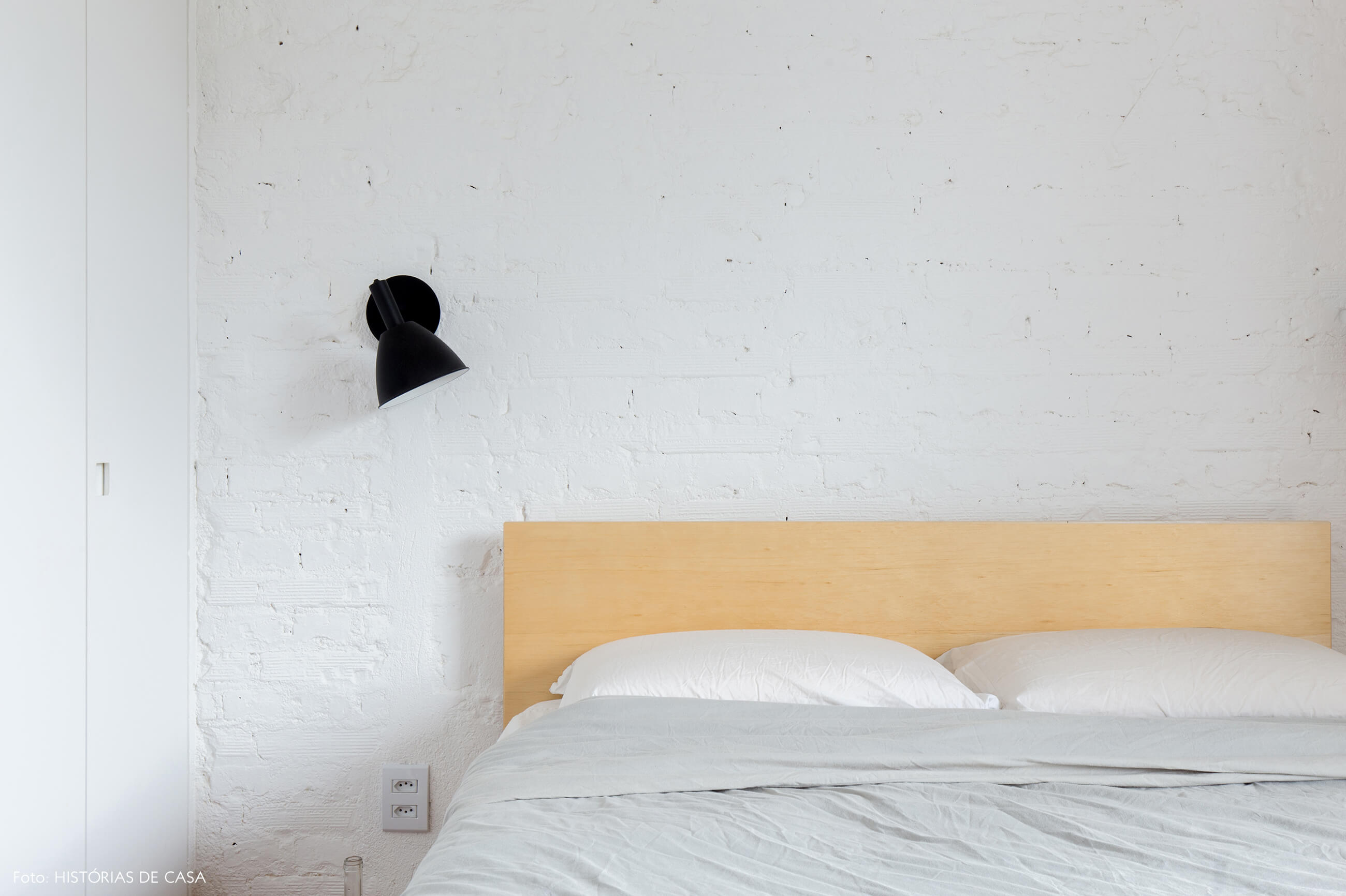 Quarto com parede de tijolinho branco e cama de madeira clara