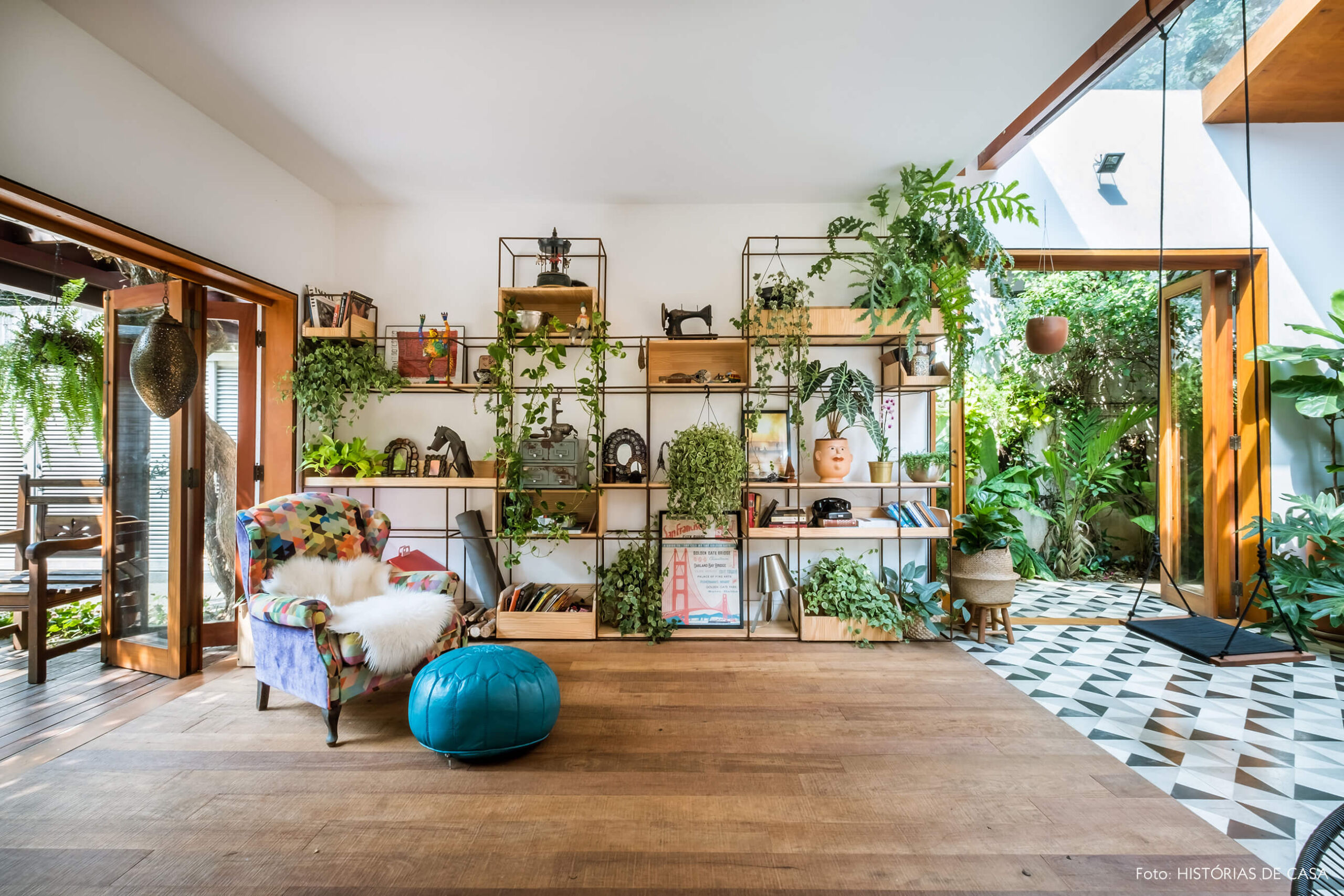Sala integrada, estante com muitas plantas e piso de madeira de demolição.