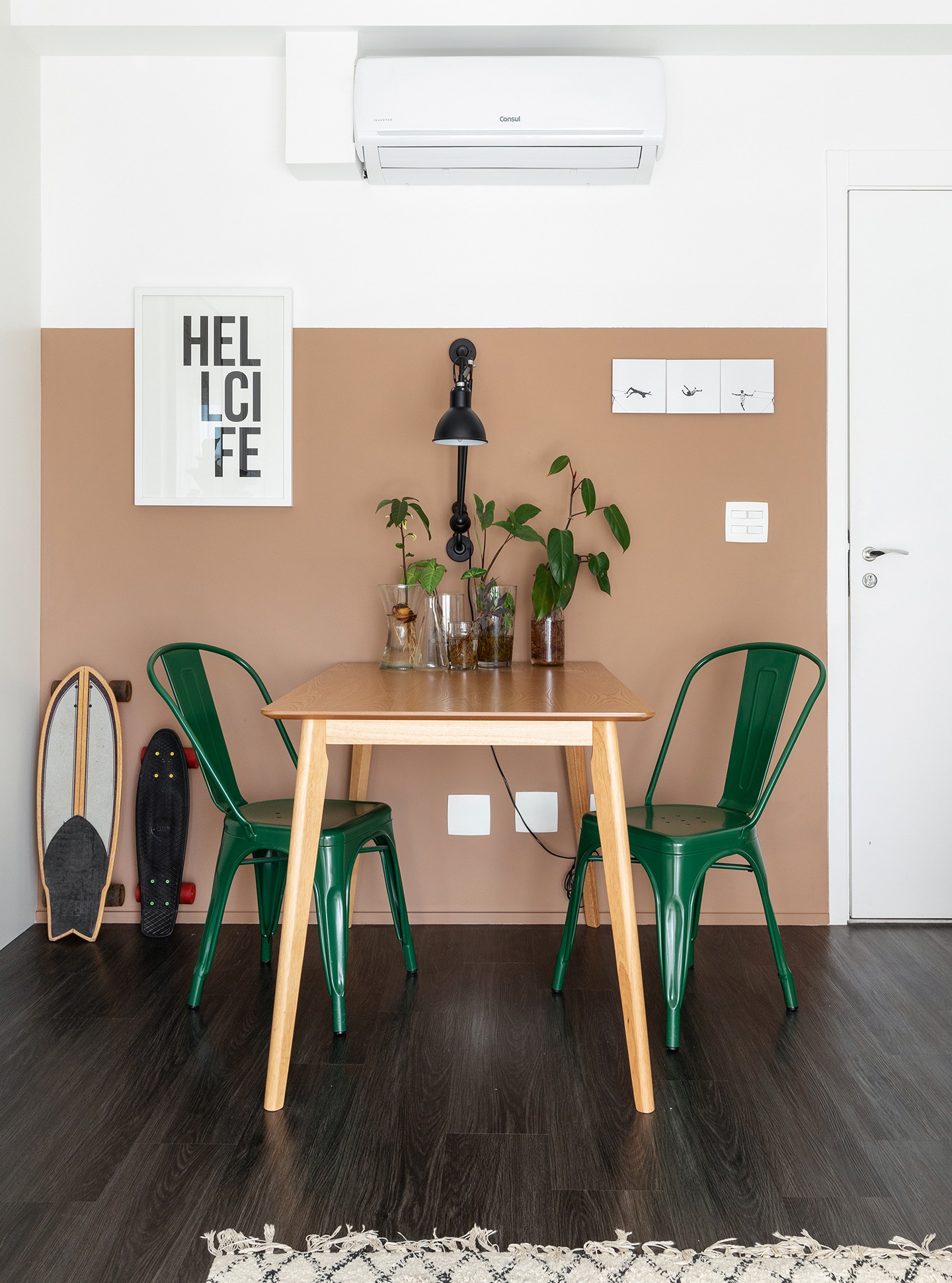 Sala com parede bege rosa com piso de madeira escura e cadeiras verdes e mesa de madeira clara