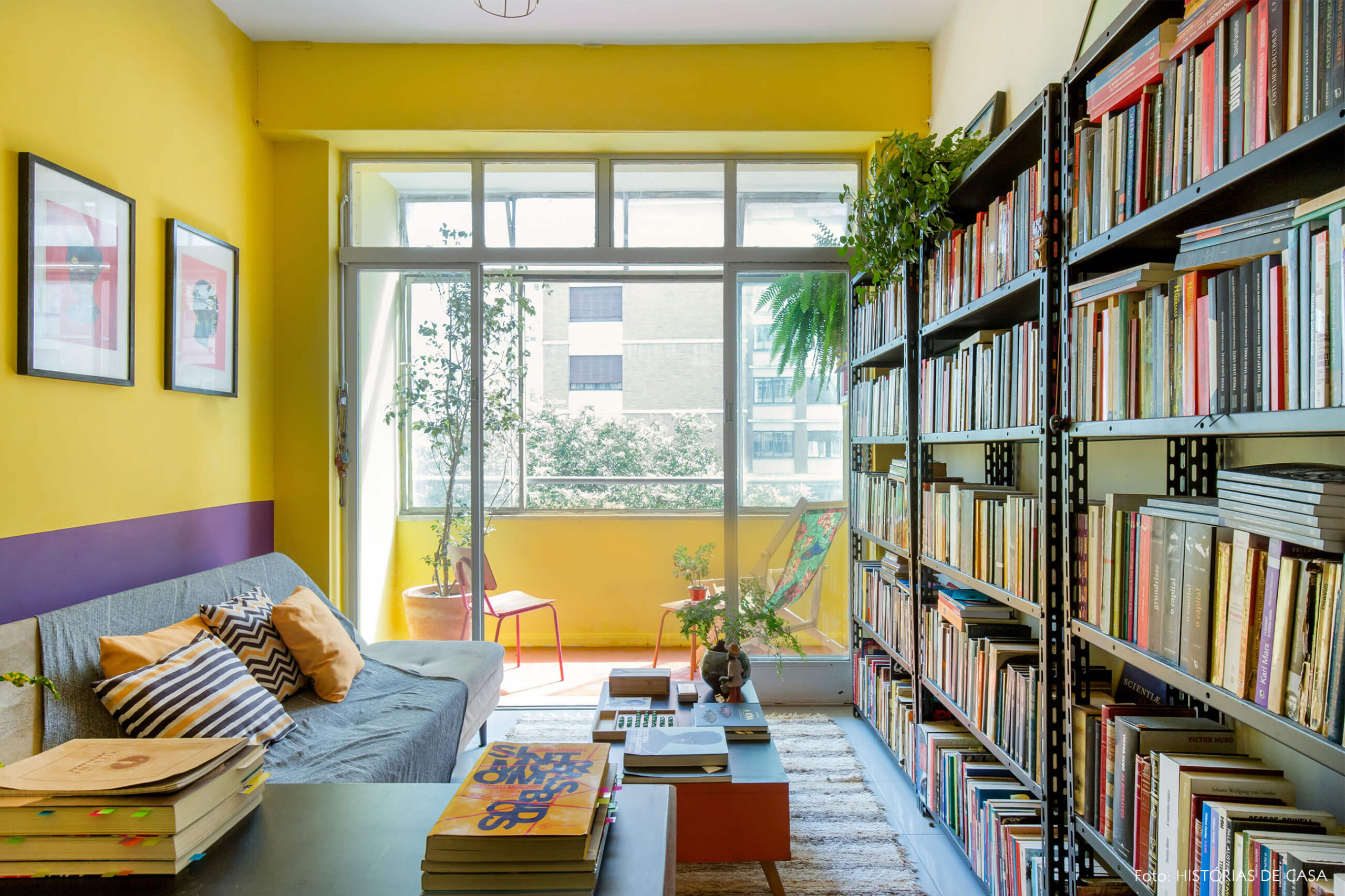 home-office-parede-amarela-e-roxa-almofadas-estampadas-amarelo-e-preto-livros-mesa-cenrto-laranja-varanda