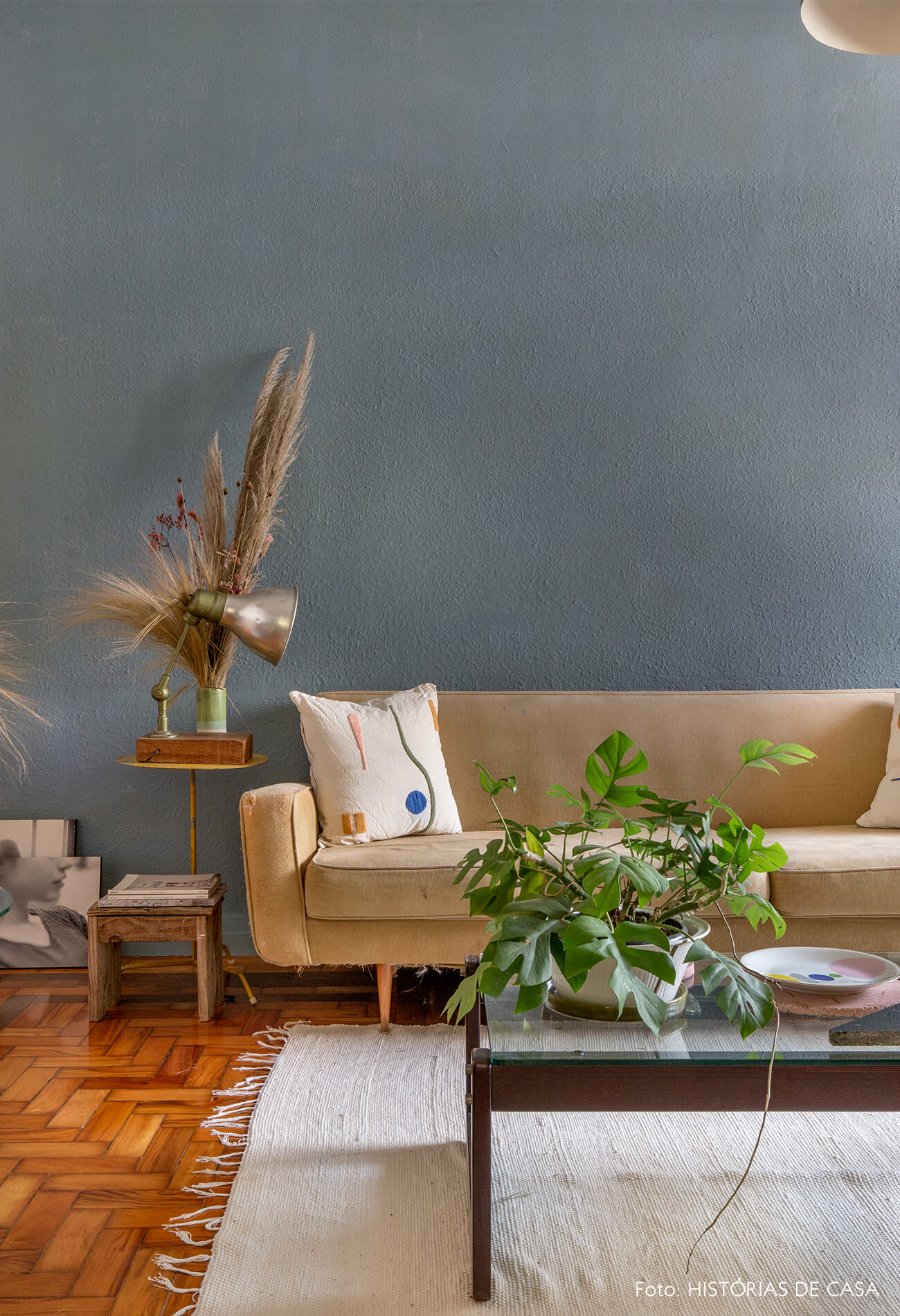Sala com parede azul e sofá bege com tapete branco e plantas