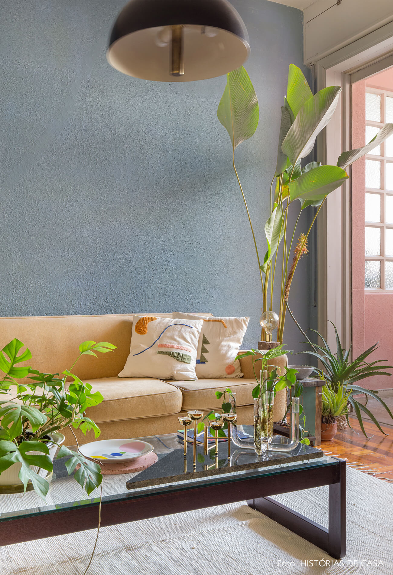 sala com parede azul piso de madeira com taepte branco e sofá bege e plantas
