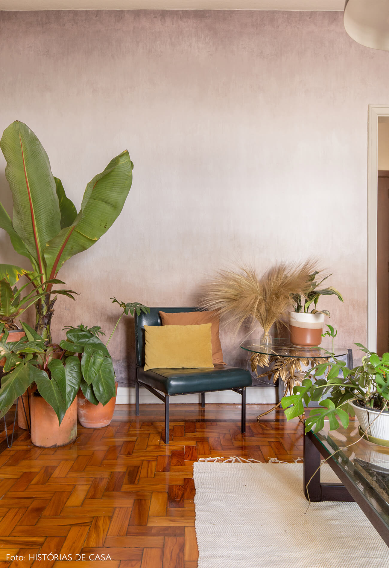 sala com parede rosa e caderia de couro com almofadas coloridas e plantas tapete branco
