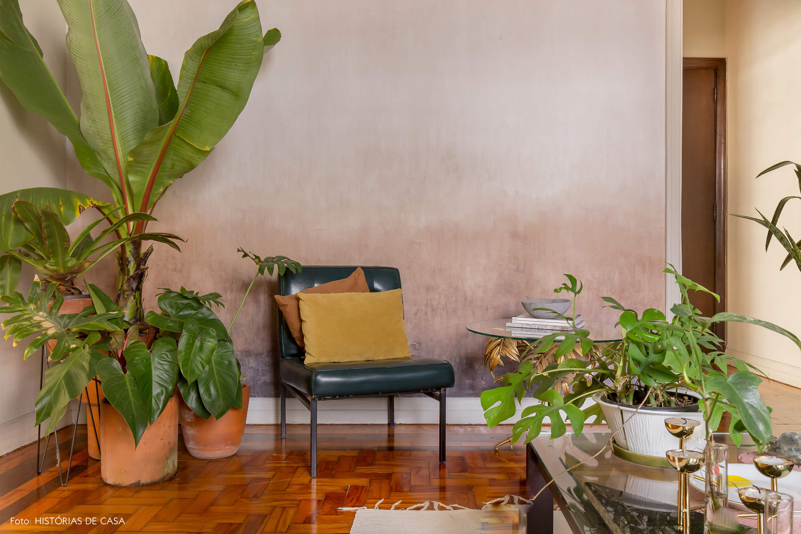 sala com parede rosa e cadeira de couro com almofadas amarela e laranja e plantas