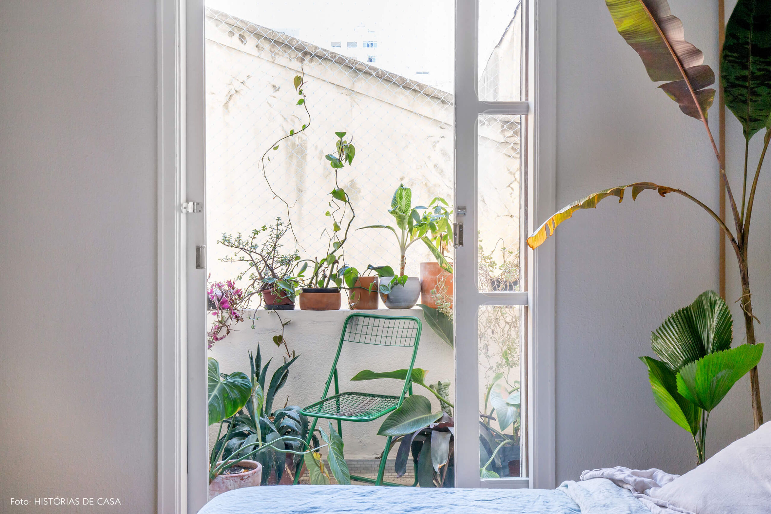 quarto com sacada e plantas paredes brancas e cadeira verde