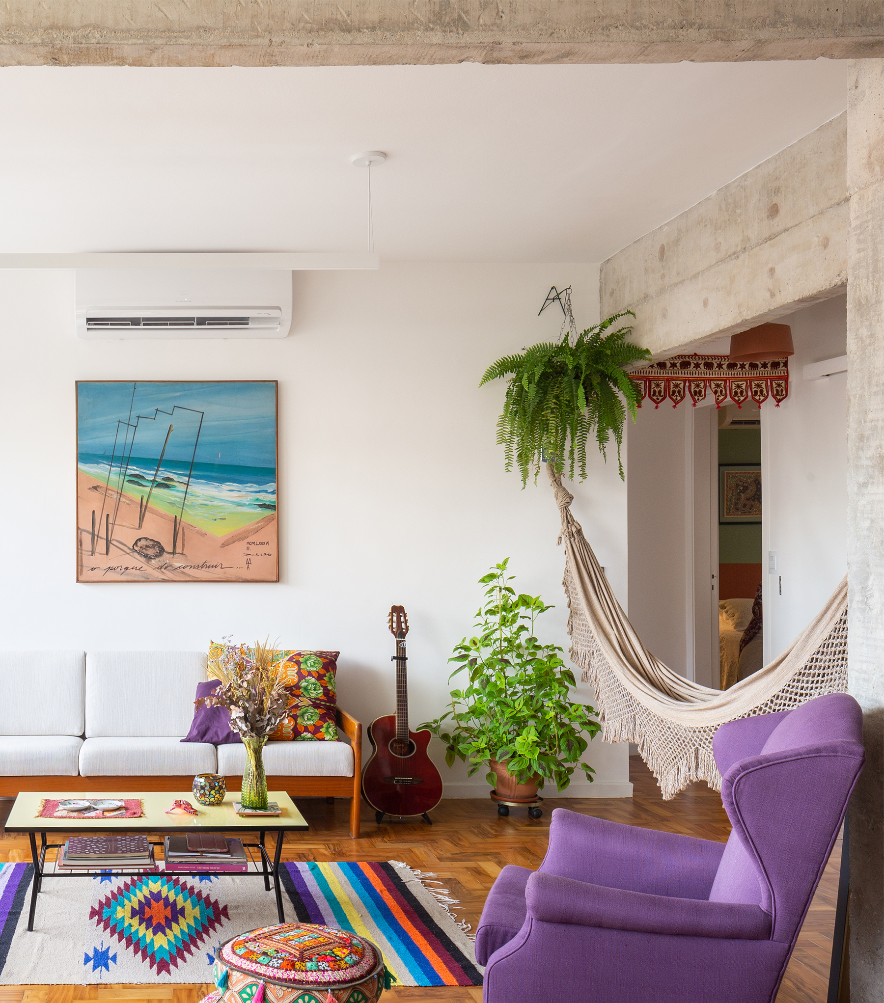 sala com poltrona roxa objetos coloridos e coluna de concreto