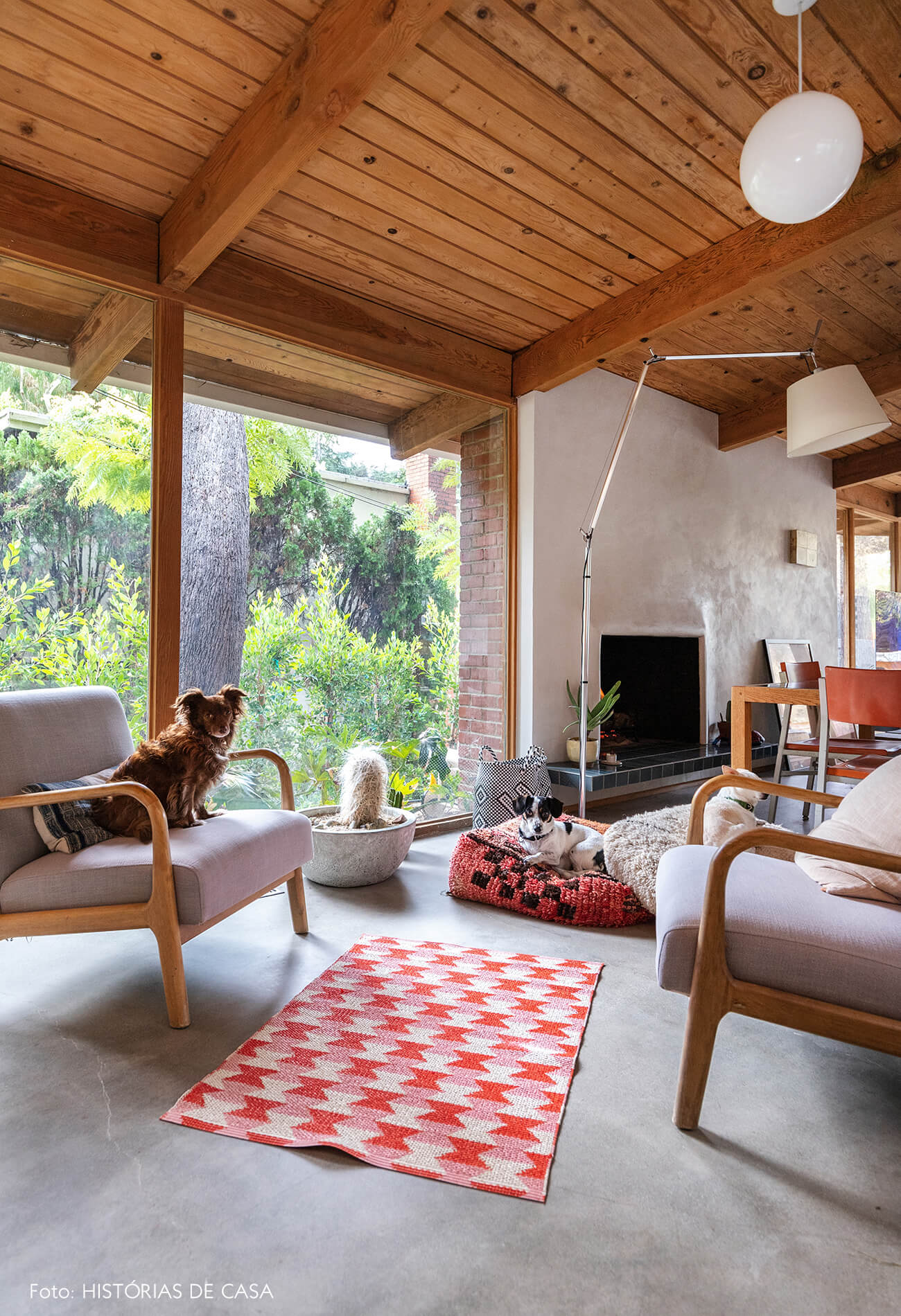 decoração casa de vidro e madeira sala com tapete vermelho poltronas claras e pufe