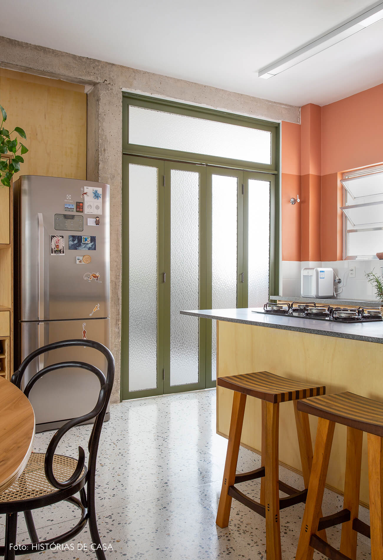 decoração cozinha com parede terrosa, porta serralheria, e cadeira thonet