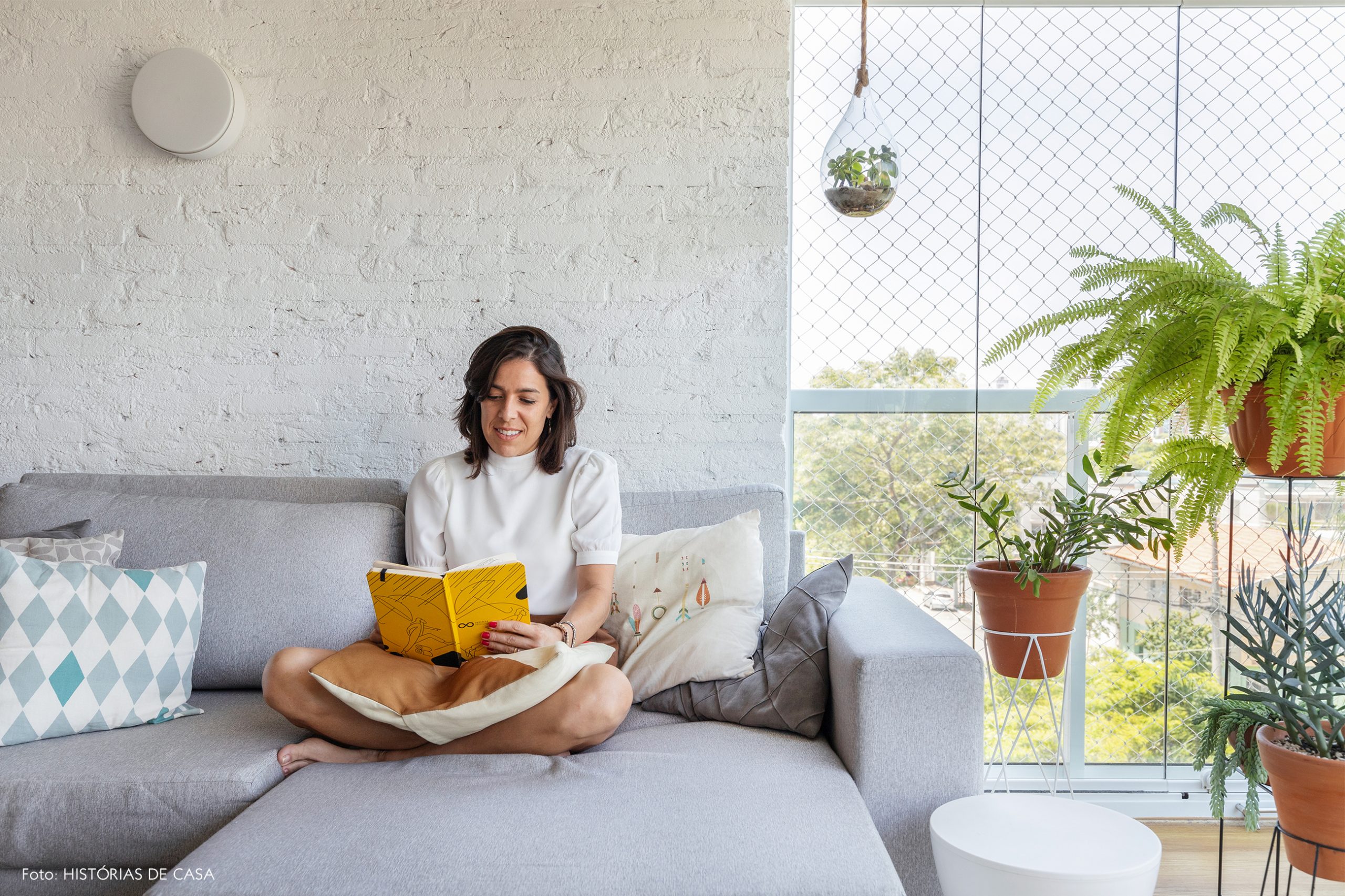 decoração retrato em sala com parede de tijolos brancos, plantas e sofá cinza