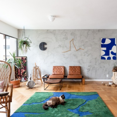 decoração sala com parede de cimento queimado tapete verde e azul e poltrona couro