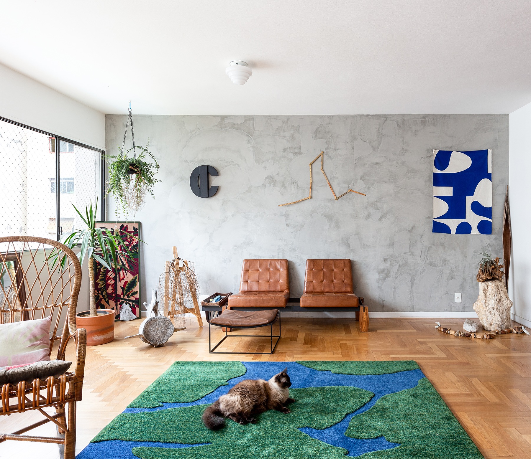 decoração sala com parede de cimento queimado tapete verde e azul e poltrona couro