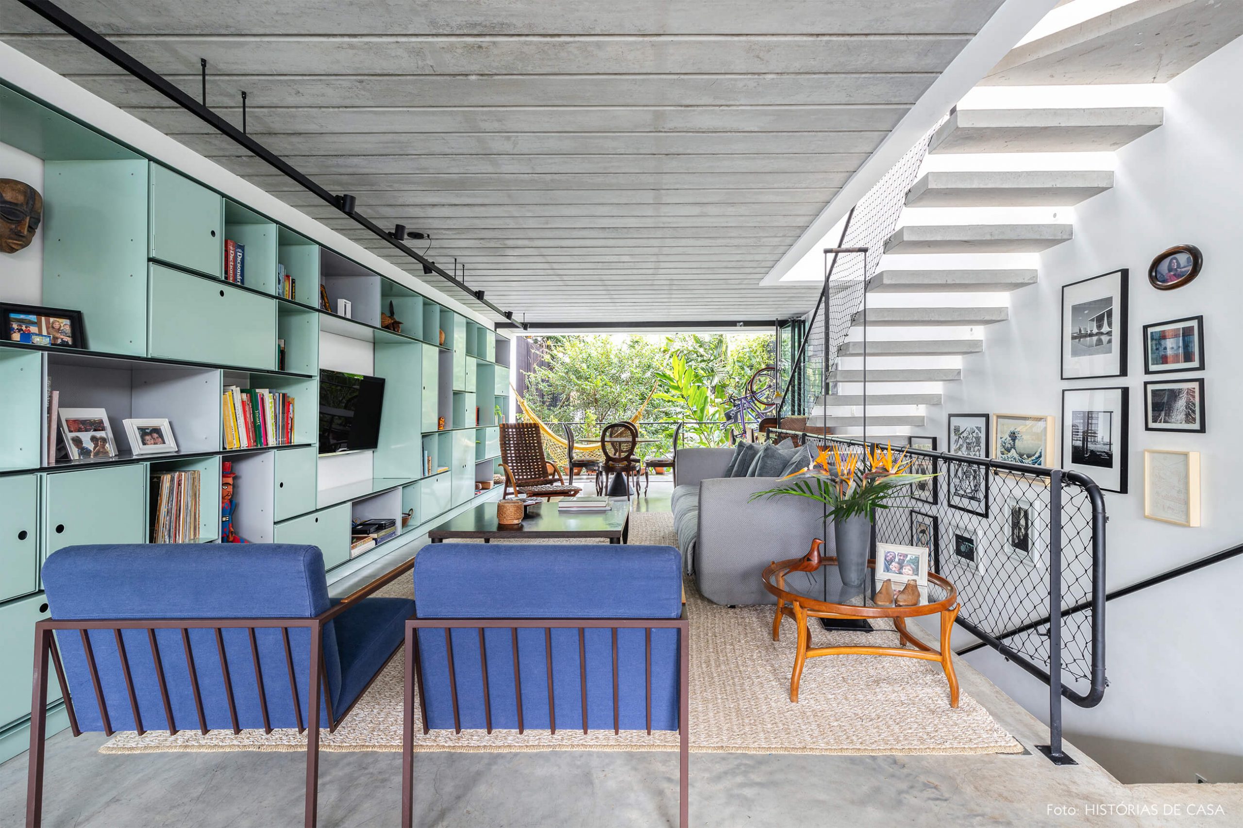 decoração casa sala com poltrona azul estante verde e escada de concreto