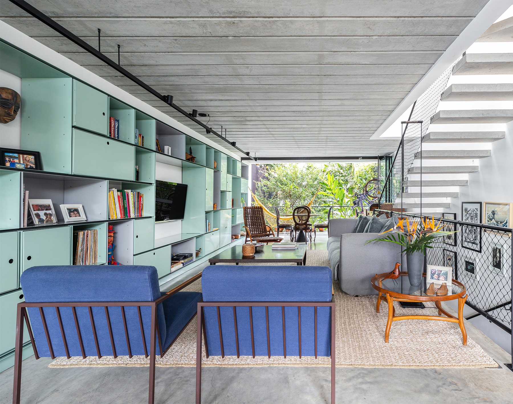 decoração casa sala com poltrona azul estante verde e escada de concreto