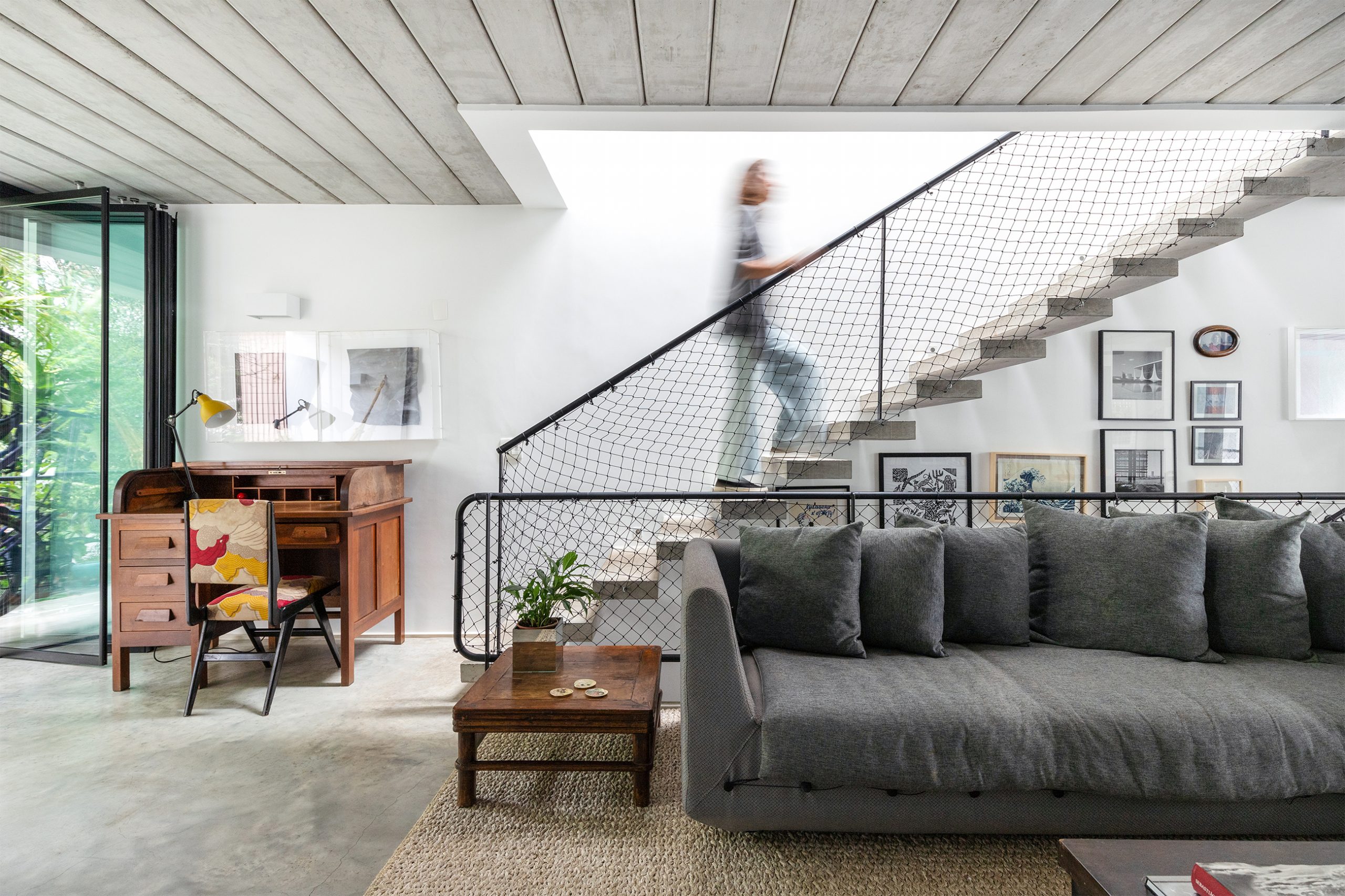 decoração casa sala com sofá cinza, escrivaninha de madeira e escada de concreto