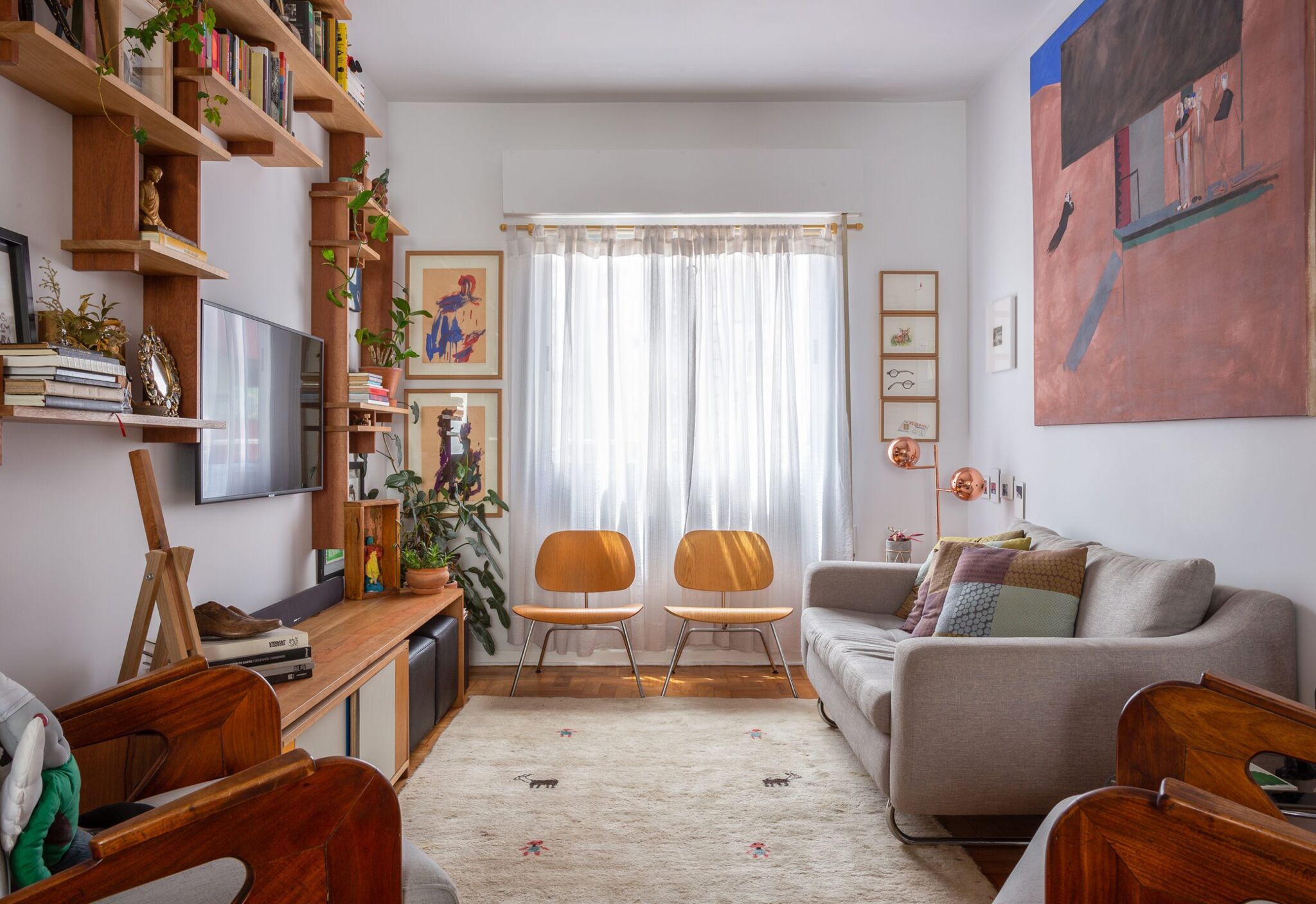 decoração sala com muitos qadros, prateleiras de madeira e cadeira eames