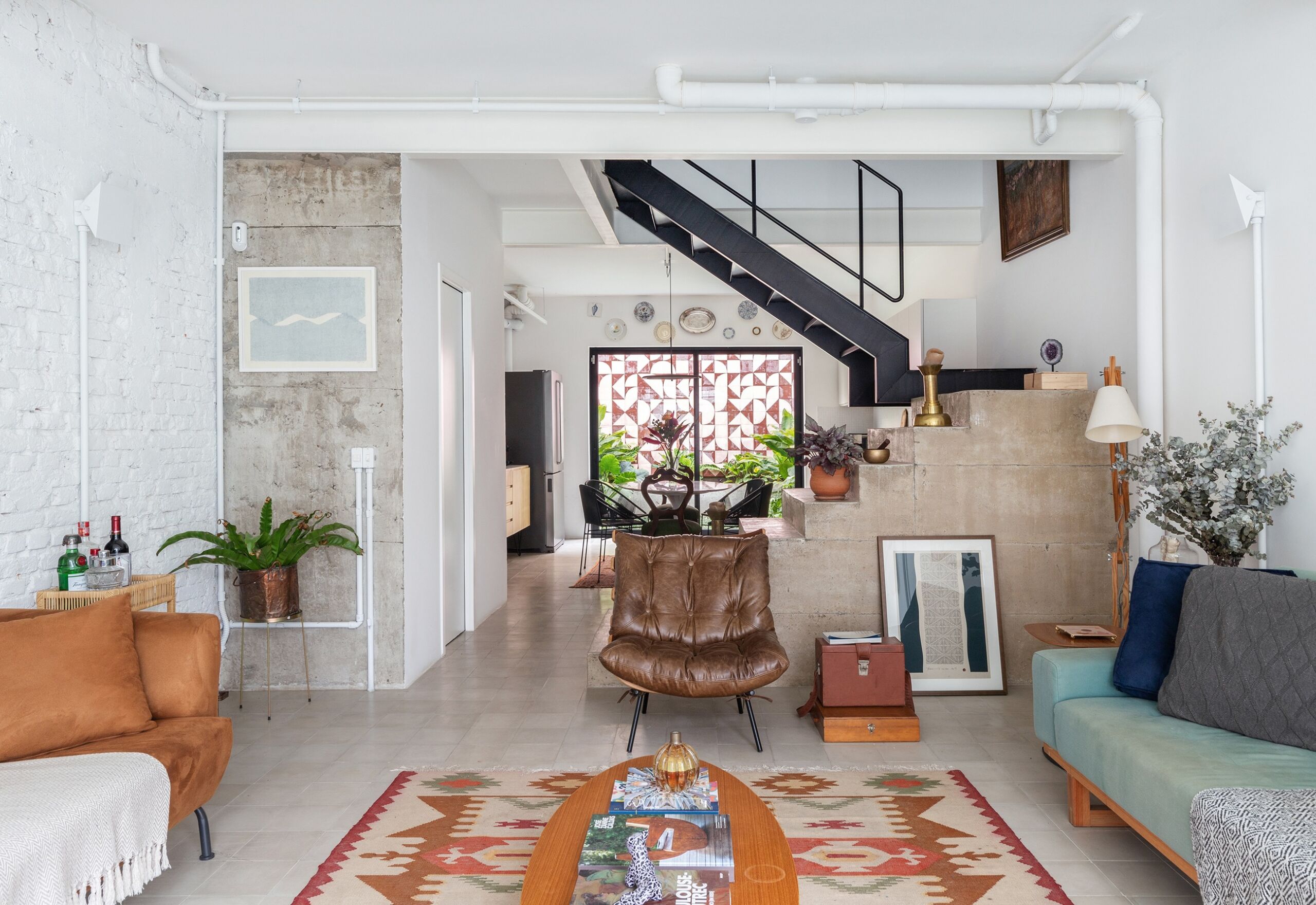 Sala integrada com escada de concreto e sofás coloridos