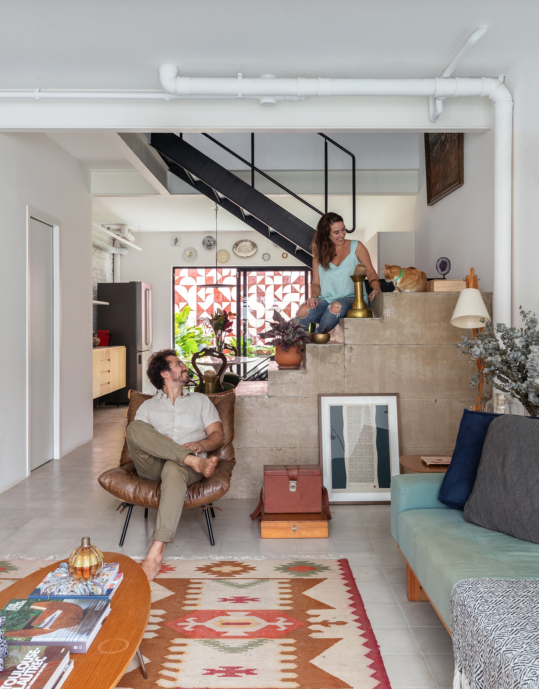 Sala integrada com escada de concreto e sofás coloridos